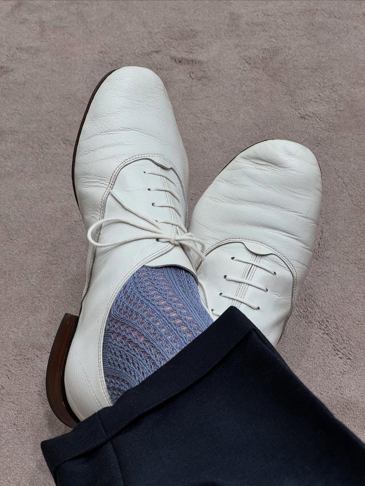 White leather oxford shoes paired with light blue patterned socks and navy trousers.