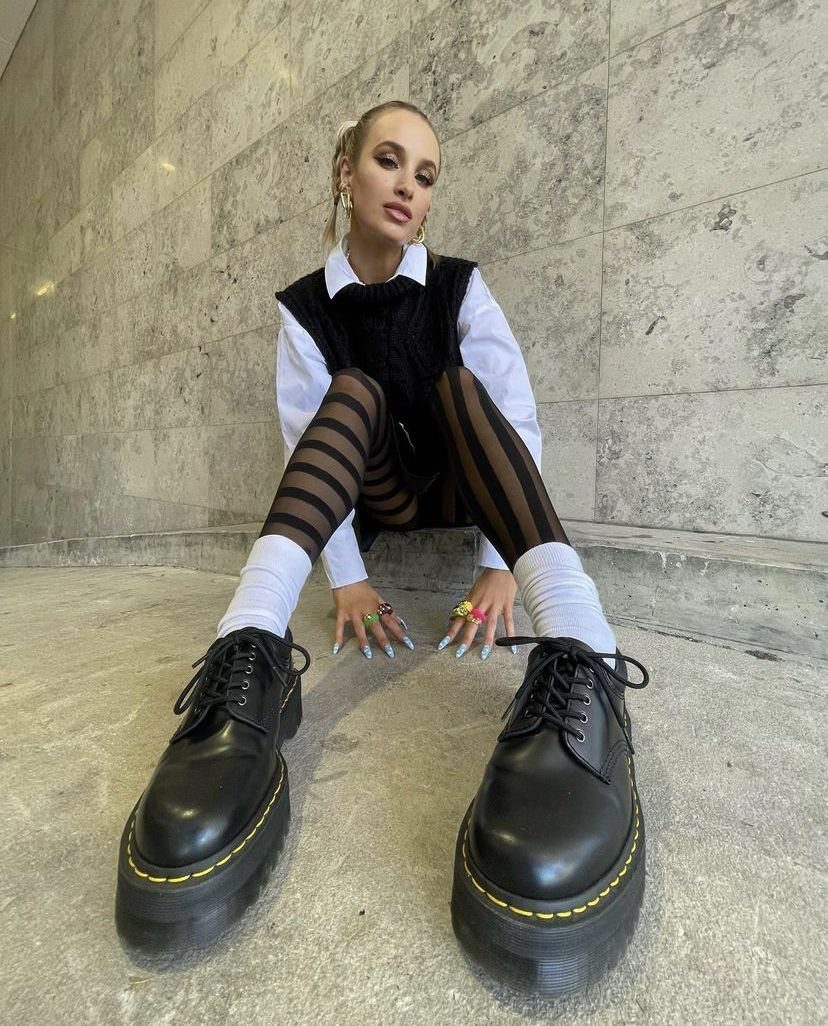 Person sitting on stone floor wearing black oxford shoes, white socks, and striped tights.