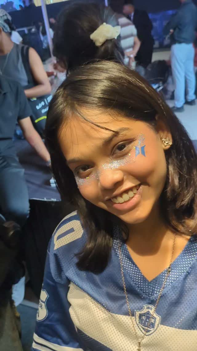 Smiling woman with white glitter applied across her cheeks and nose wearing a blue jersey.