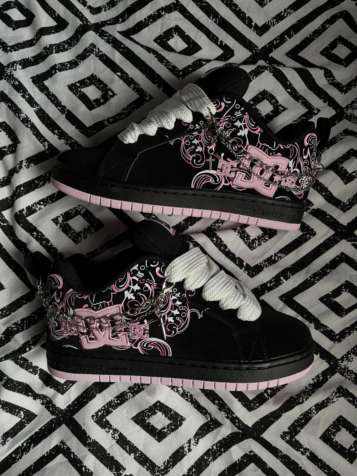Black chunky sneakers with pink floral designs and white laces on patterned fabric.
