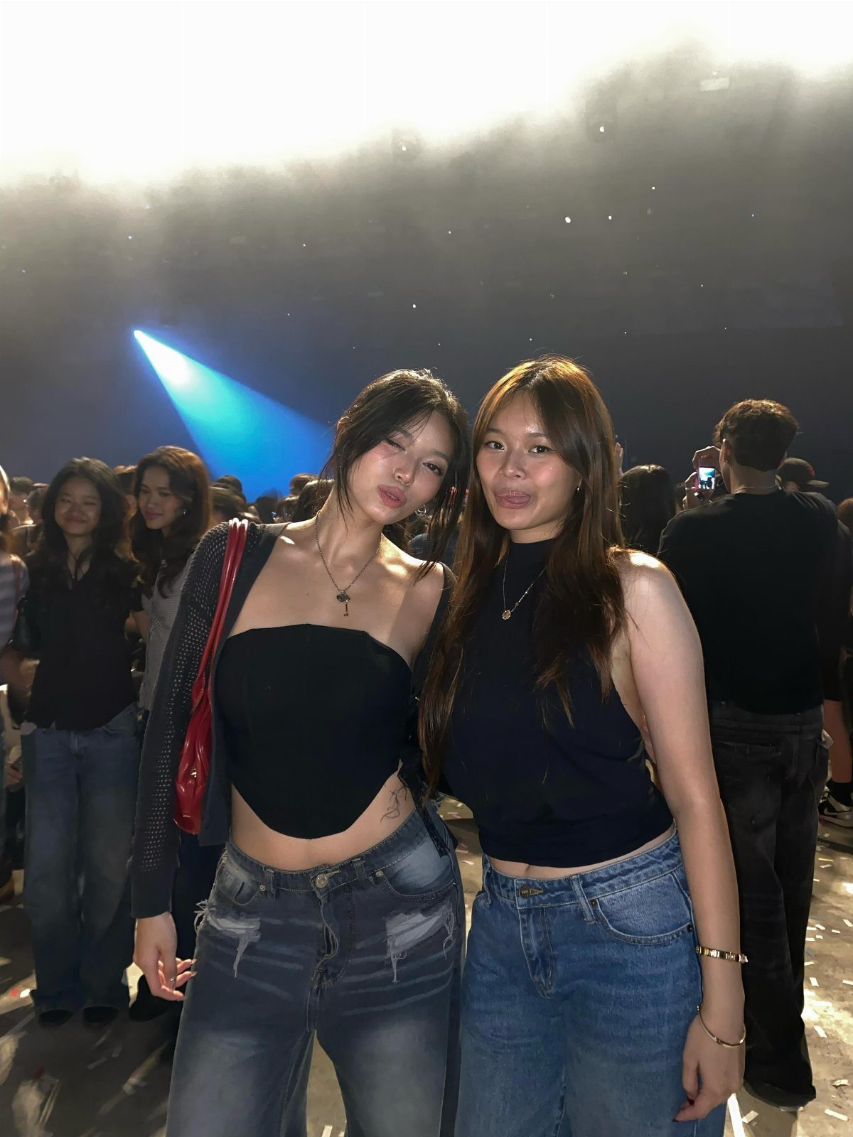 Two young women posing in crop tops and high-waisted jeans at a concert.