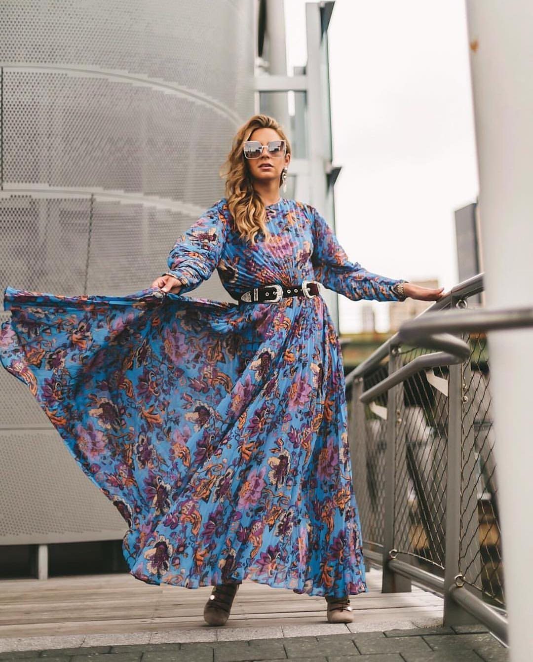 Woman in a blue patterned flowy maxi dress standing on an outdoor walkway.