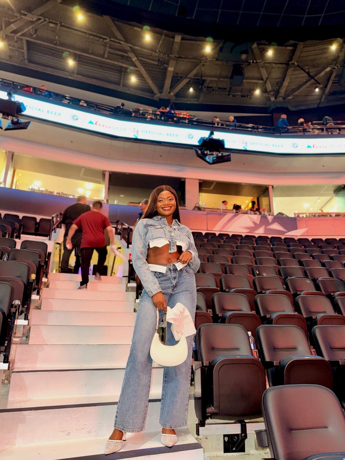 A woman posing in a denim jacket and wide-leg denim jeans inside a large stadium.
