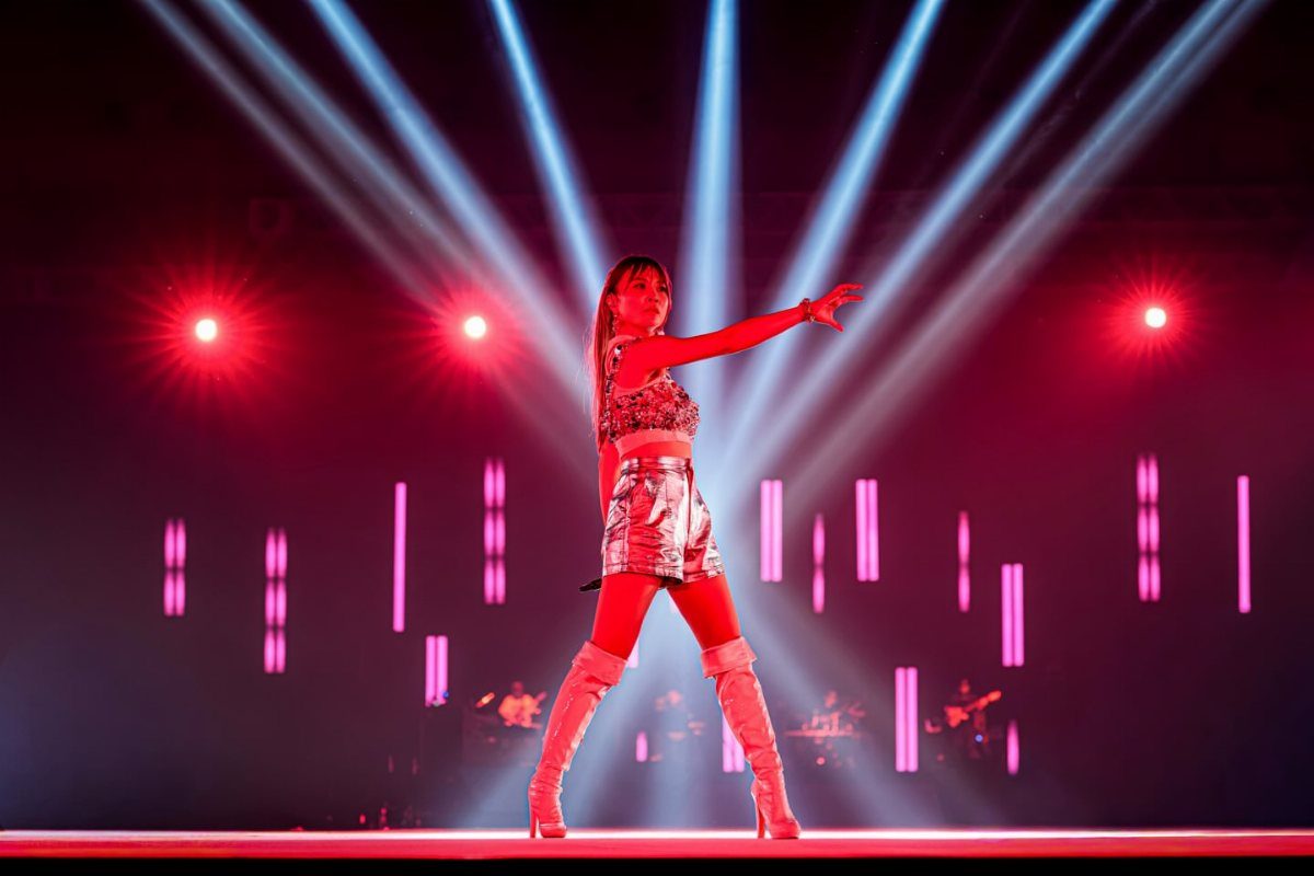 A performer wearing a metallic silver top and high-waisted shorts on a lit stage.