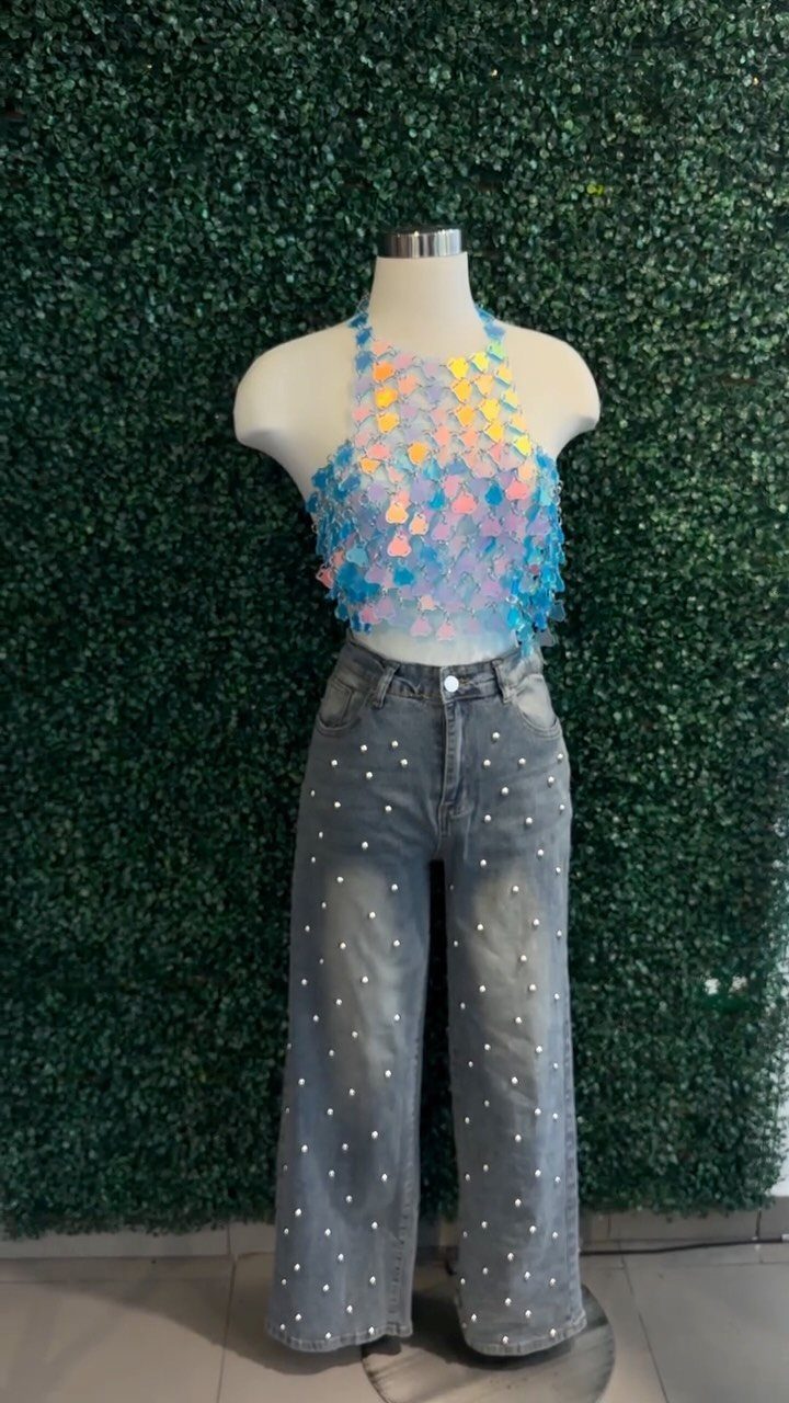 Mannequin wearing a sequined halter top and pearl-embellished wide-leg denim jeans against a green hedge.