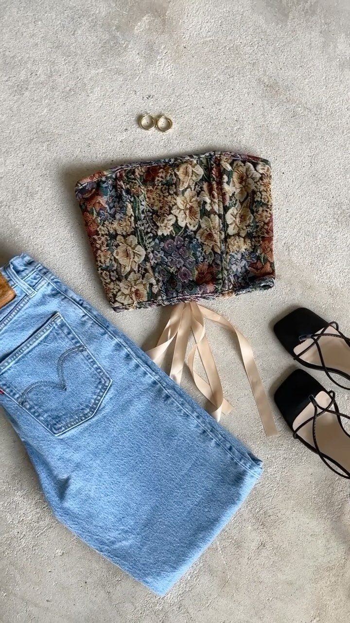 Floral corset top, denim shorts, gold rings, and black lace-up flats laid on a stone surface.
