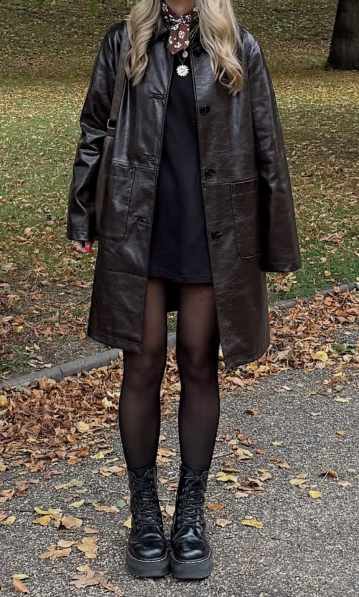 A person wearing a dark brown leather coat, black dress, black tights, and black boots.