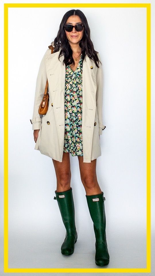 Woman wearing a floral dress, beige trench coat, and tall green rain boots.