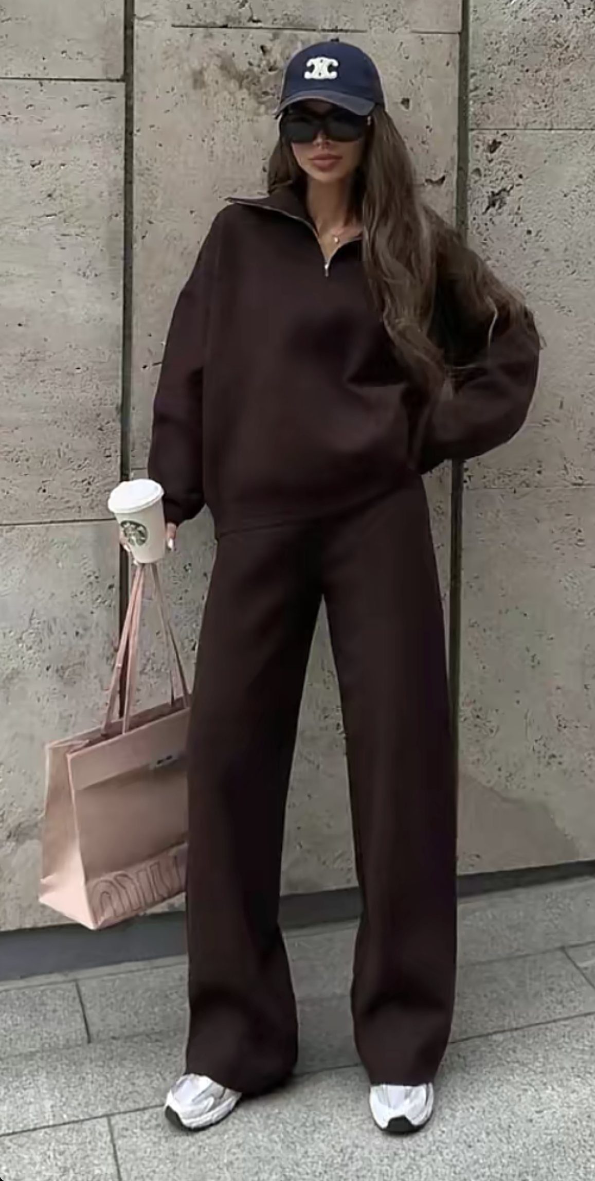 A woman posing in a dark brown matching pullover and wide-leg pants set with a baseball cap.