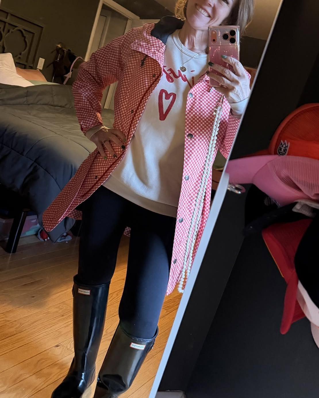 Woman in a checkered parka, white heart sweatshirt, black leggings, and black rain boots.