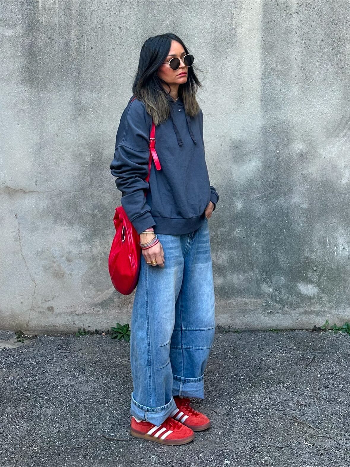 Woman in a grey hoodie and wide blue jeans wearing bright red sneakers.
