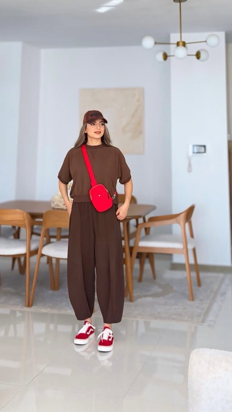 Woman in brown coordinated outfit and red sneakers standing in a modern dining room.