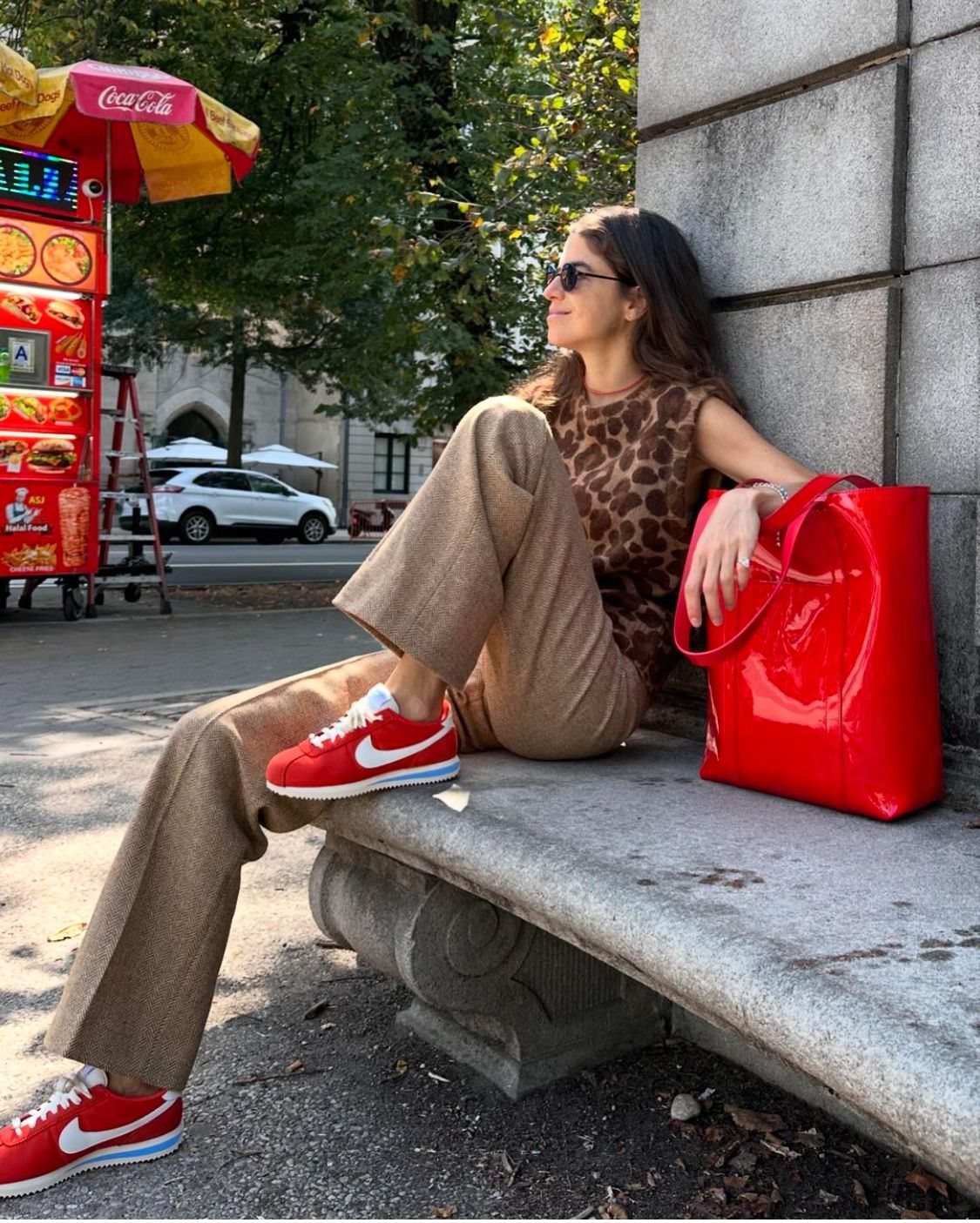 Woman in leopard print top and tan trousers sitting on a stone ledge wearing red sneakers.