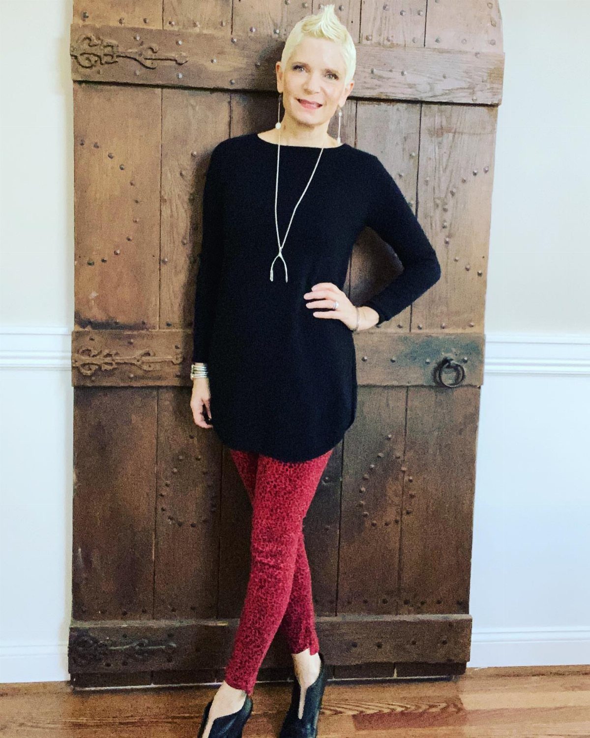 Woman posing in a long black tunic, red patterned trousers, and black heels.
