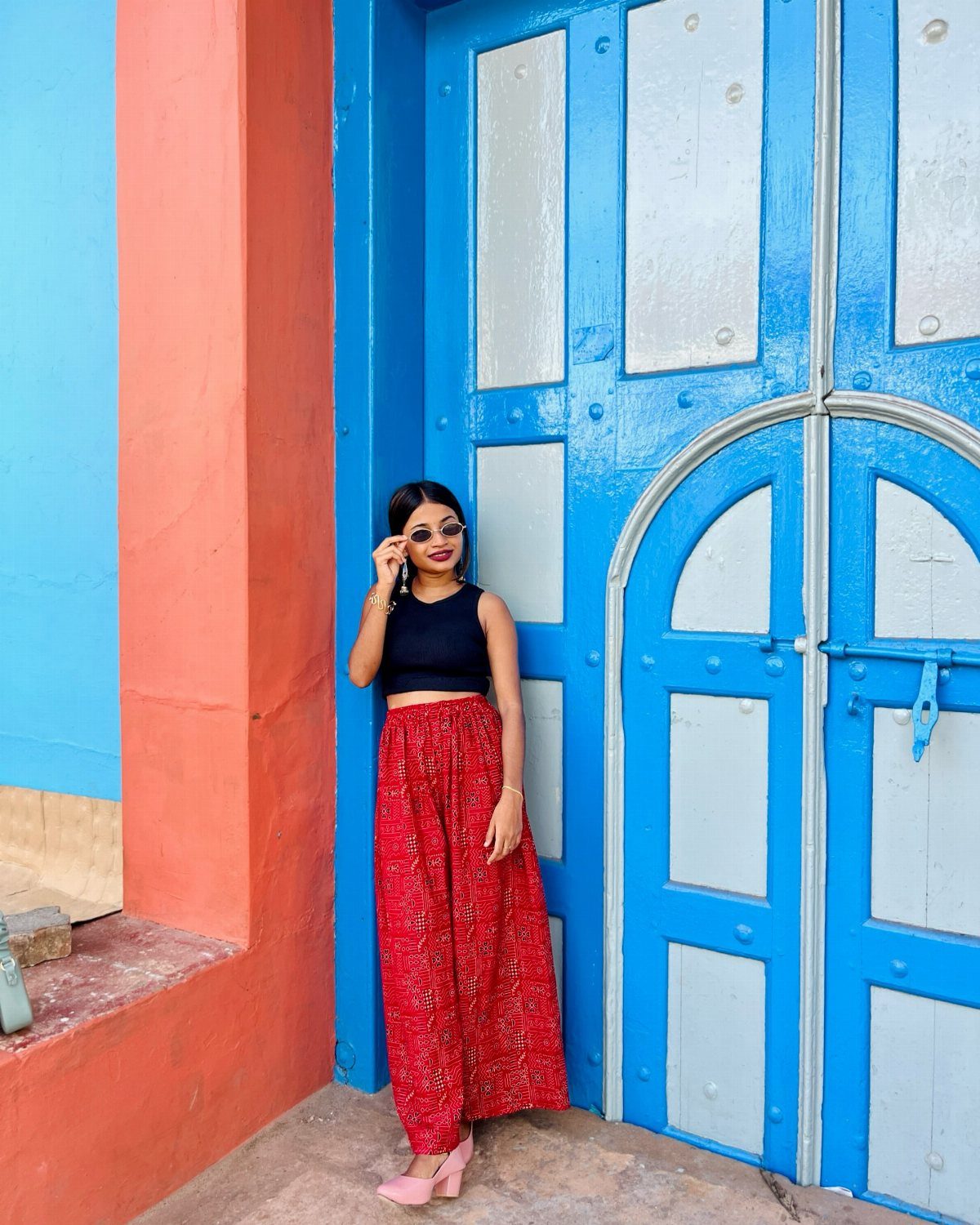 Woman wearing a black crop top and high-waisted red trousers standing by a blue door.