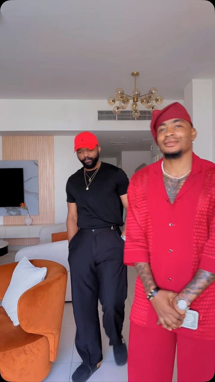 Two men posing in a living room wearing black and red outfits.