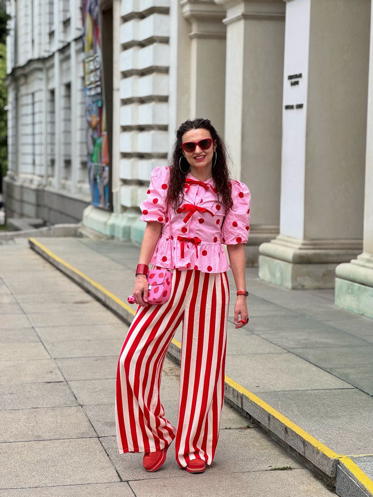 A woman posing in a pink polka dot top and red and white striped trousers.