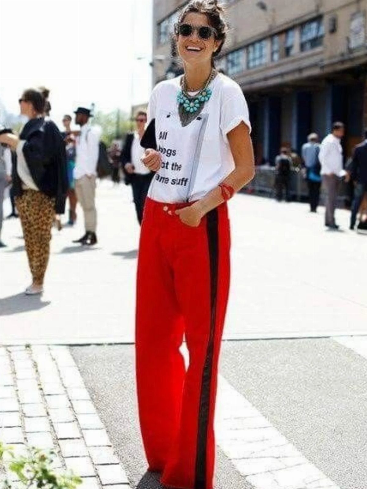 Woman in a white t-shirt and red wide-leg trousers walking on a sunny city street.