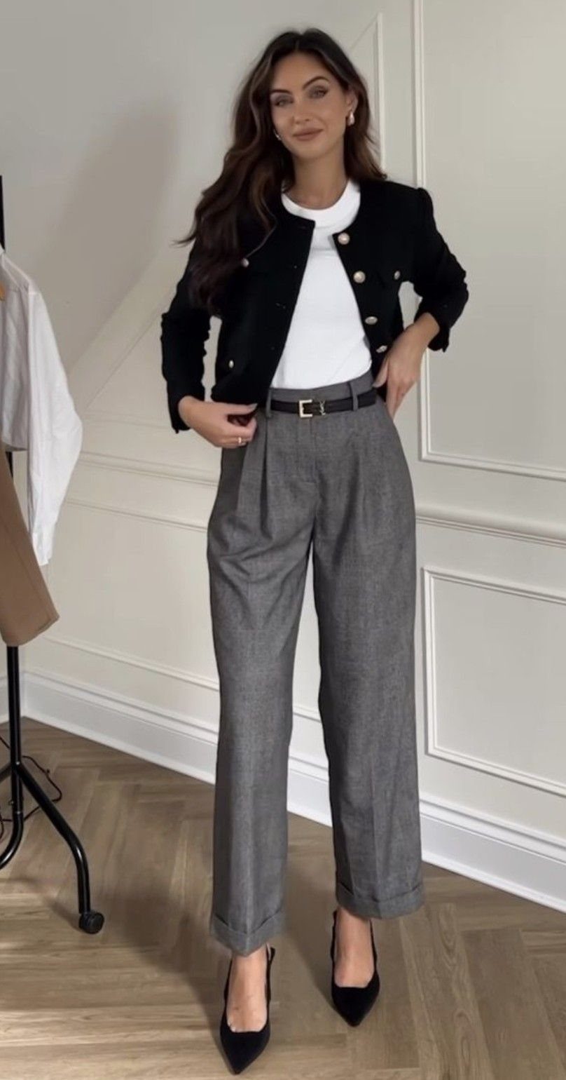 Woman wearing a black jacket, white top, grey trousers, and black heels.
