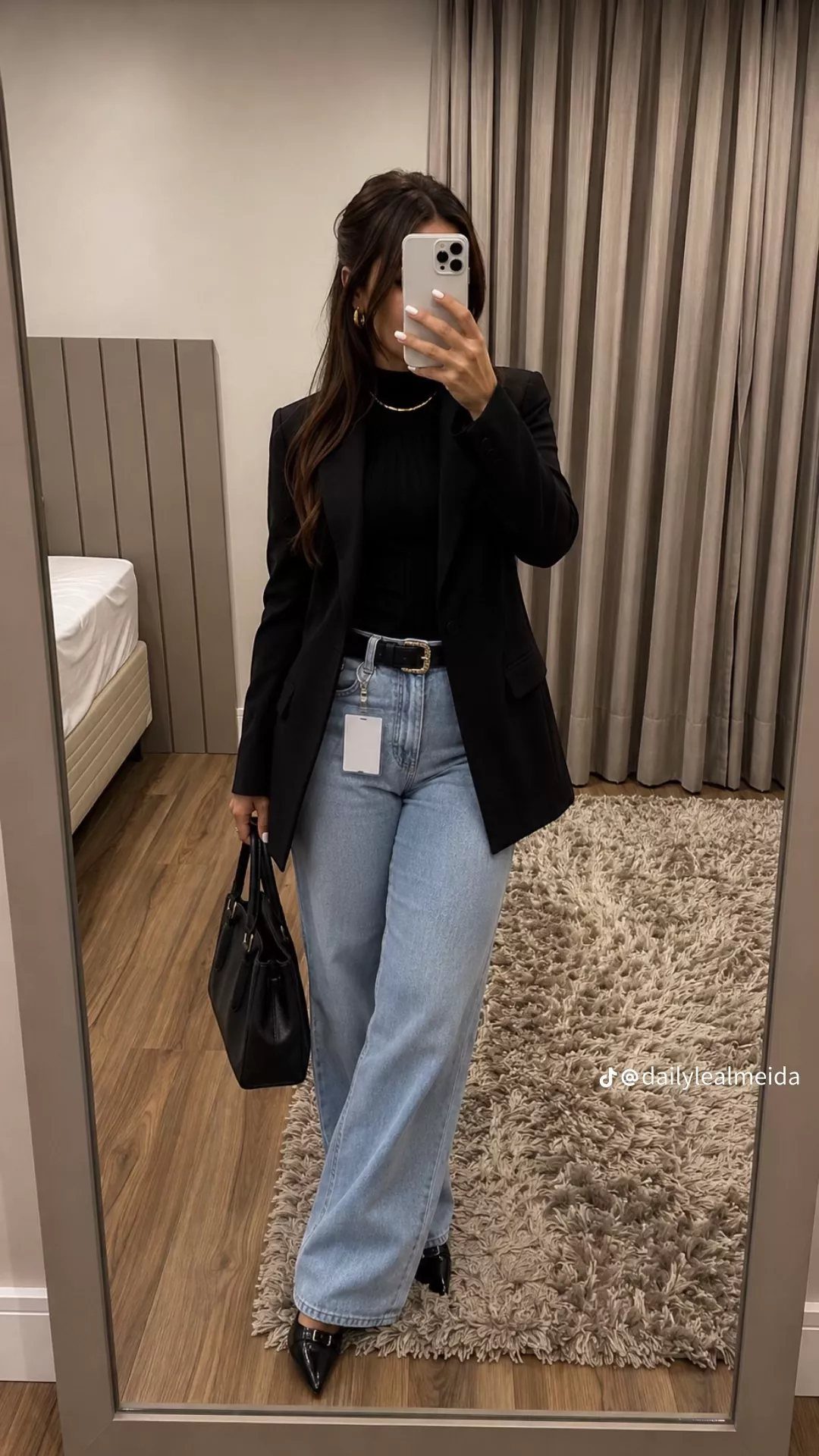 Woman in a black blazer, black turtleneck, and light blue wide-leg jeans posing in a mirror.