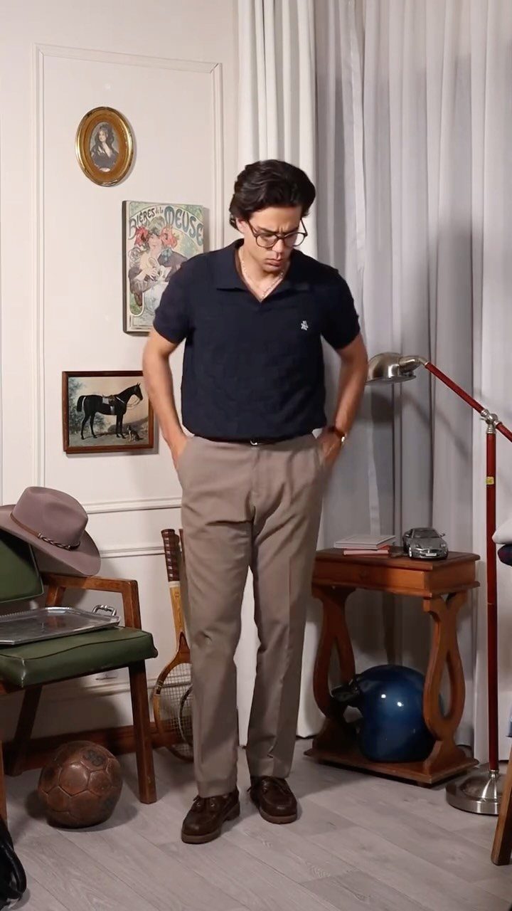 Man wearing a navy polo shirt and tan trousers standing in a room.