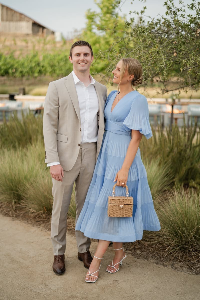 A man in a tan suit and a woman in a blue dress posing outdoors.