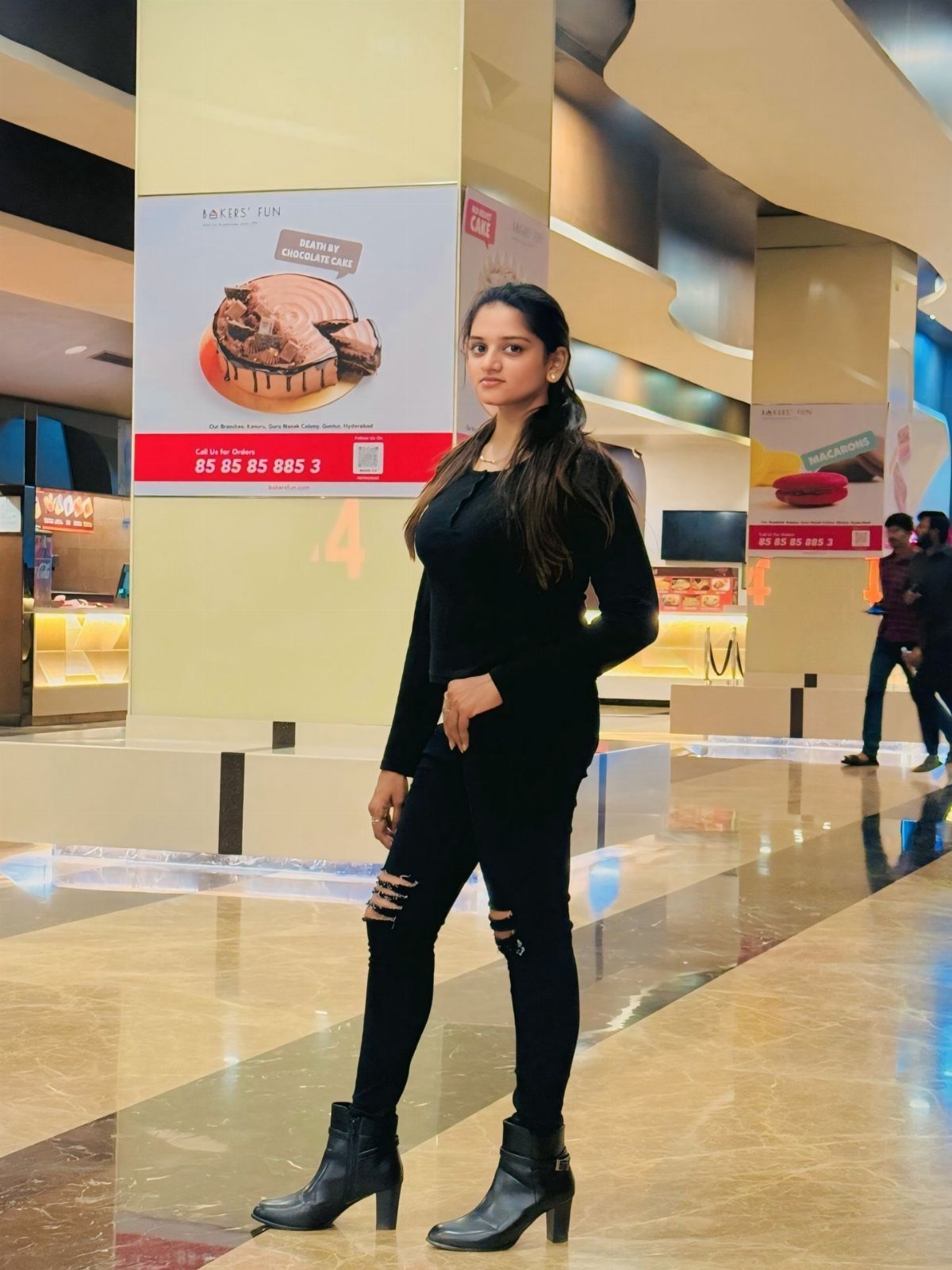 A woman wearing black ripped jeans and black leather ankle boots standing in a mall.