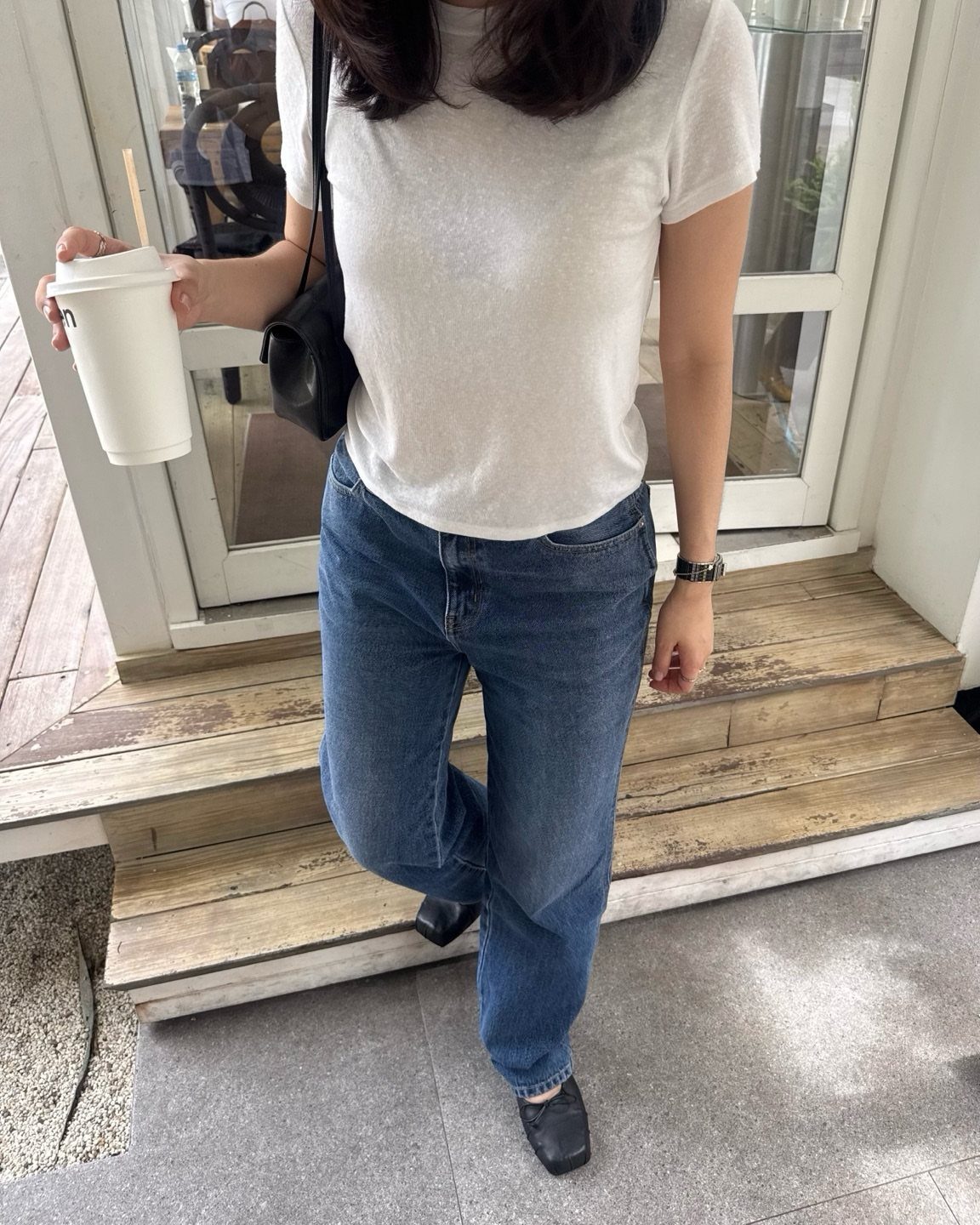 A person wearing blue jeans and black ballet flats standing on wooden steps.