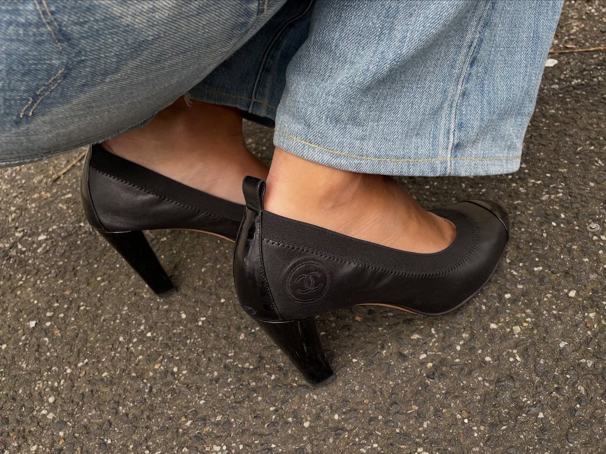 Black high-heeled pumps worn with blue denim jeans on asphalt.