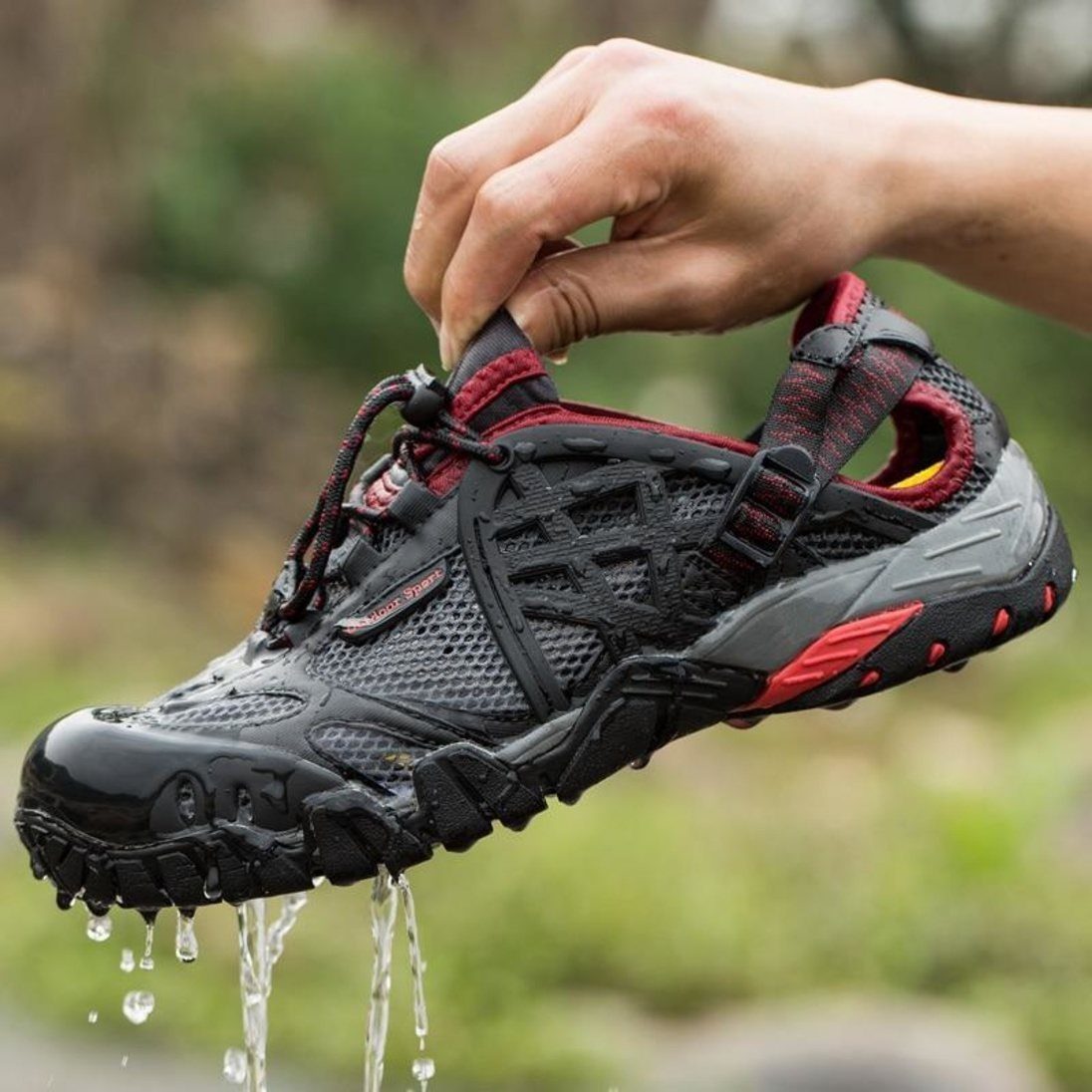 A hand holds a wet black and red sport sandal dripping with water droplets.