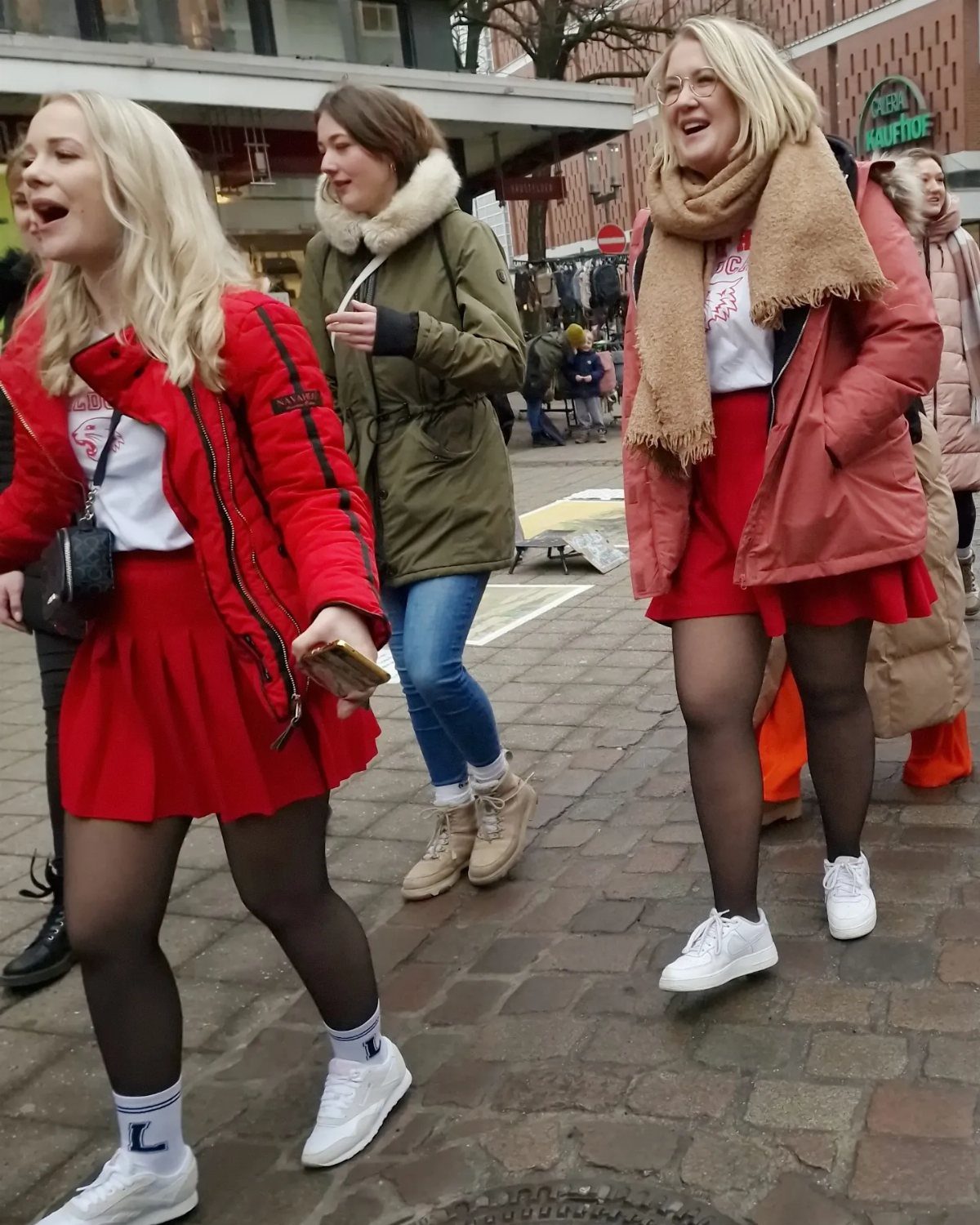 Two women walking down a street wearing colorful jackets, skirts, and sneakers.