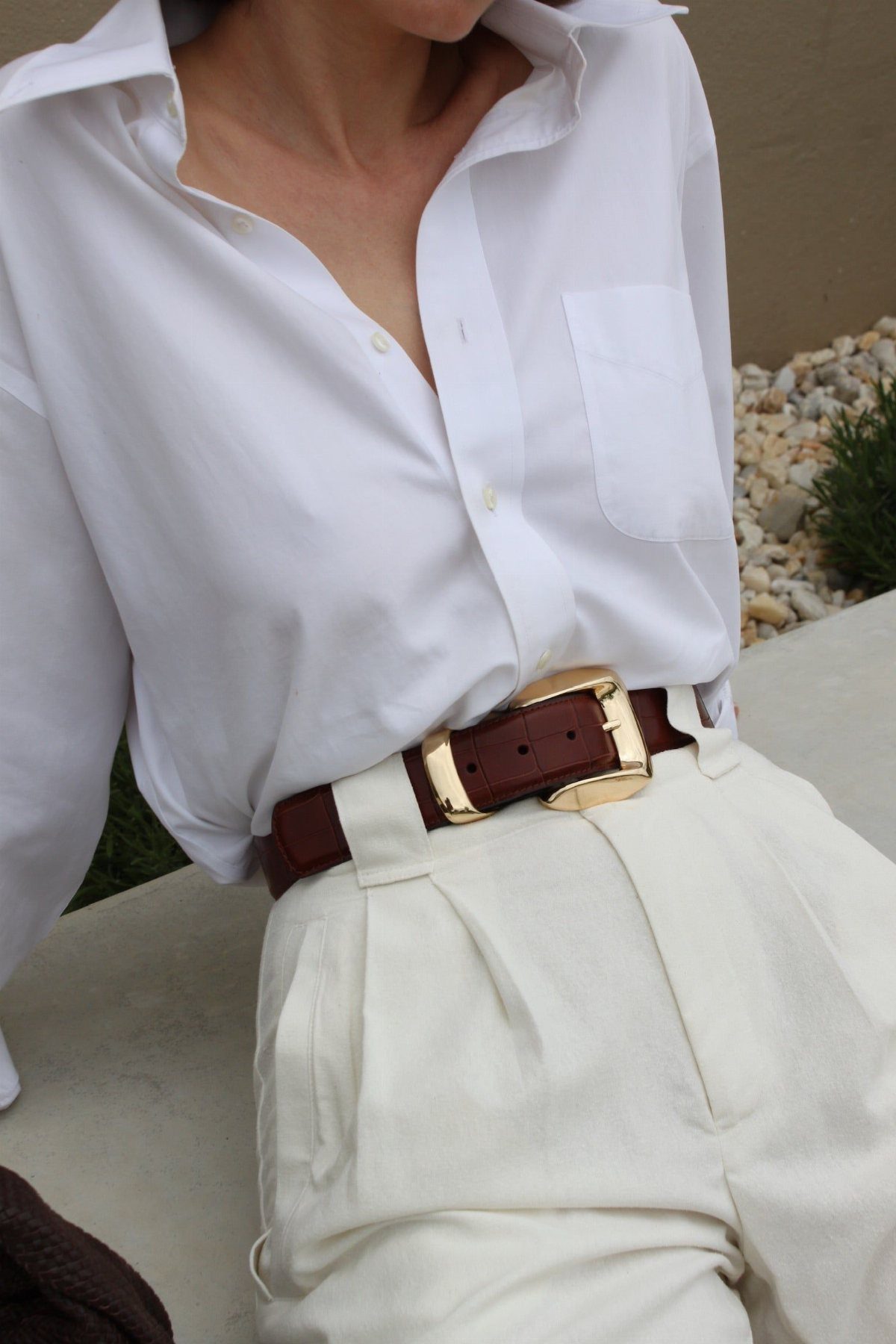 Person wearing a white button-down shirt, cream trousers, and a brown leather belt with a gold buckle.