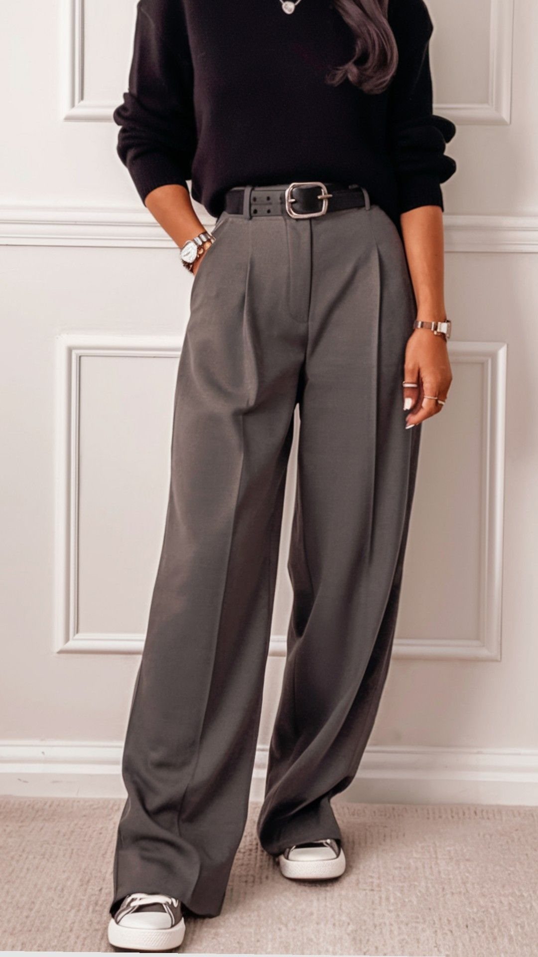 Woman wearing wide-leg grey pleated trousers, a black top, and white sneakers.