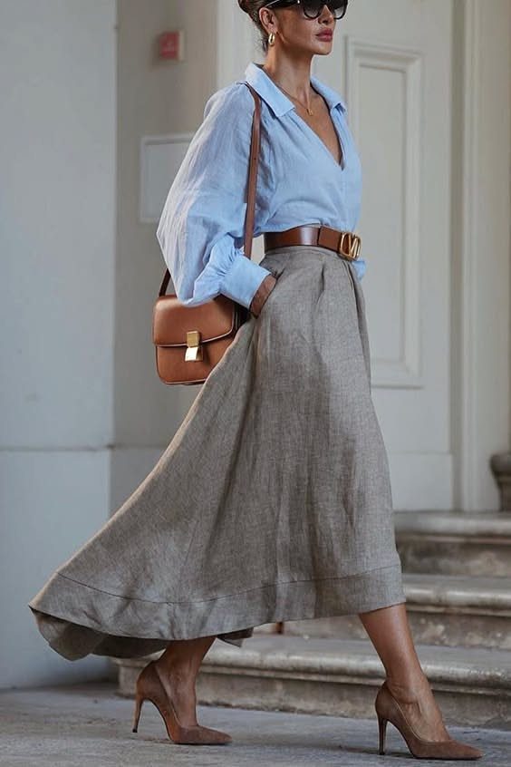 Woman walking in a blue shirt, long grey skirt, and brown high heels.