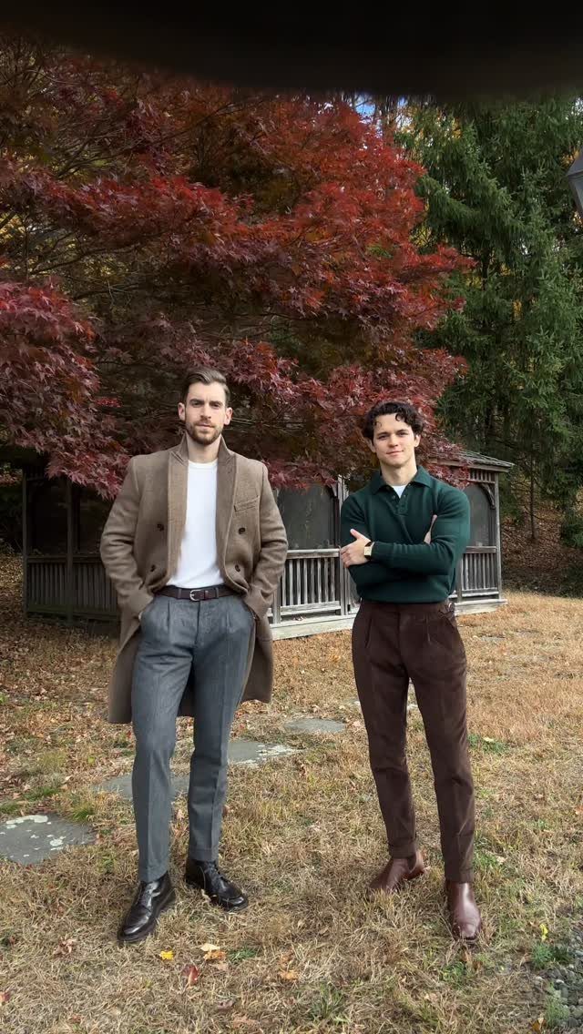 Two men posing in smart casual autumn outfits standing in front of red autumn trees.