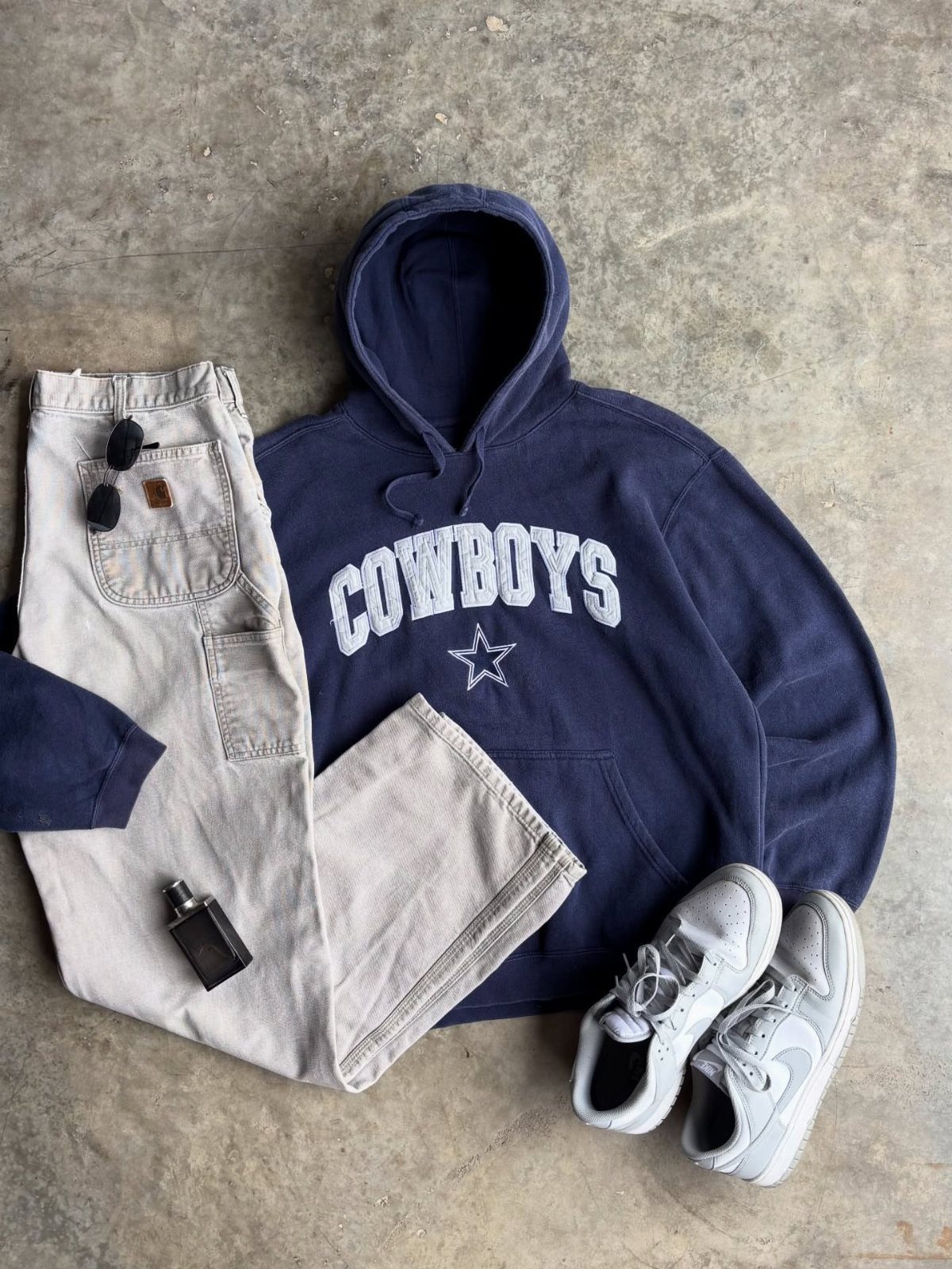 Navy blue Cowboys hoodie, beige cargo pants, and white sneakers laid out on concrete.