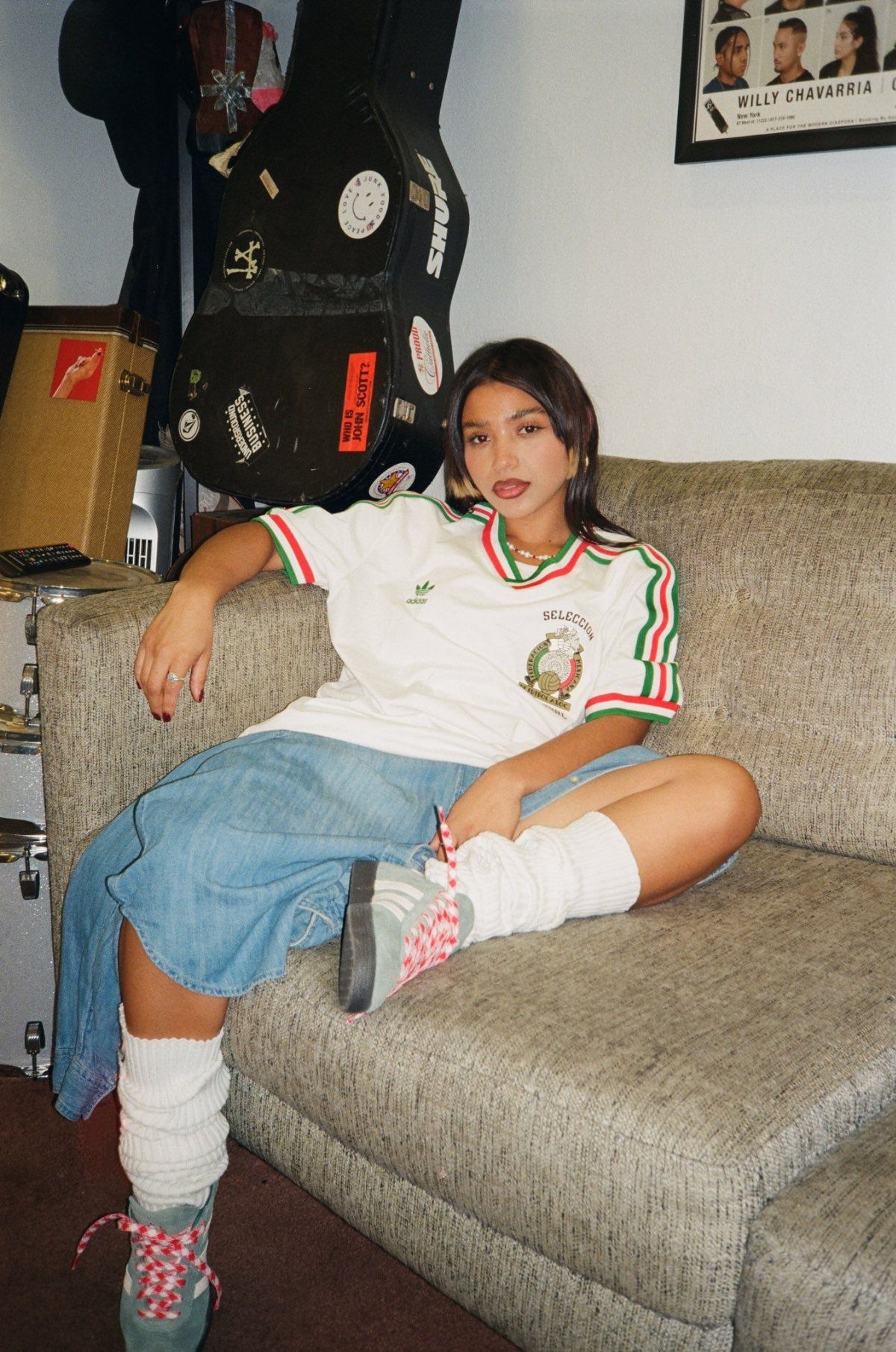 Woman in a white striped jersey, denim skirt, and retro sneakers sitting on a sofa.