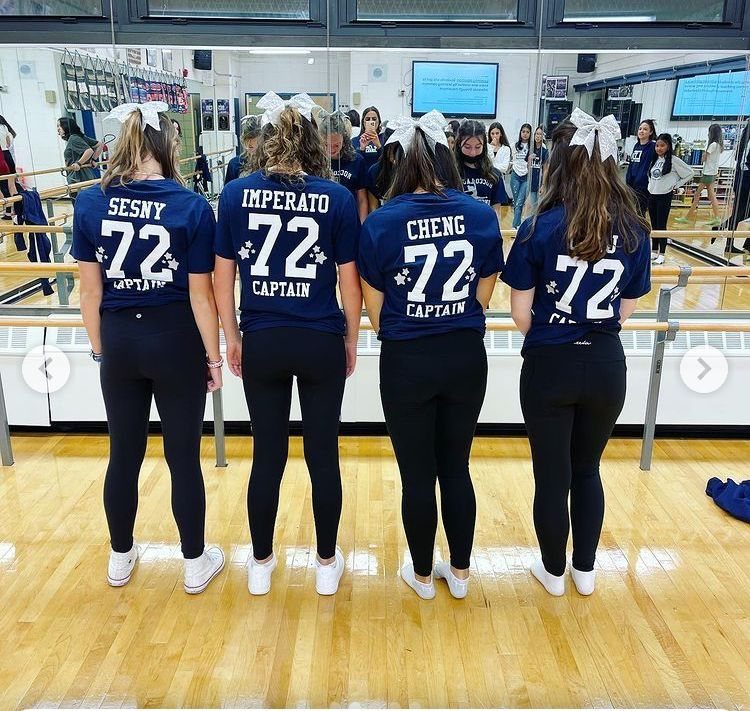 Four women standing in a gym wearing navy blue team shirts and black leggings.