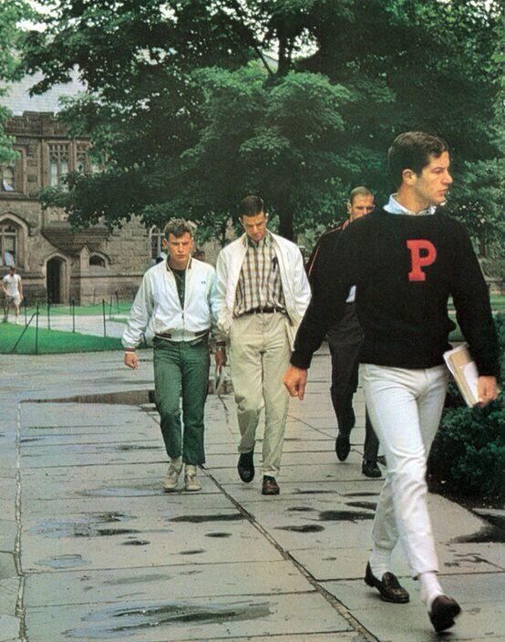 Young men walking outdoors, featuring a man in a black varsity sweater and loafers.