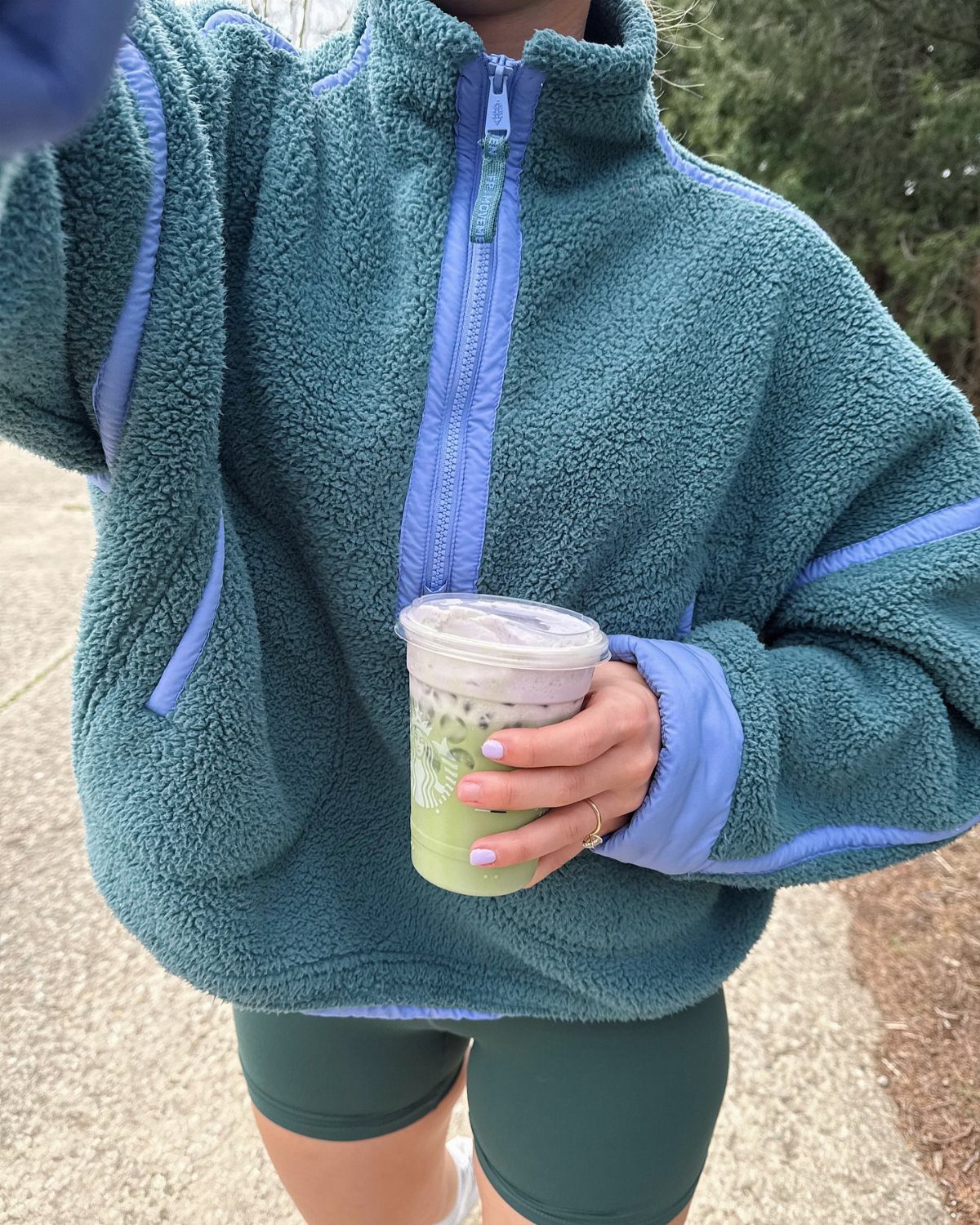 Person wearing a teal fleece jacket and green athletic shorts holding a green drink.