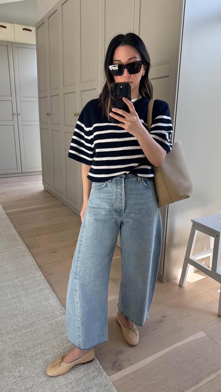 Woman in striped short sleeve sweater, wide-leg denim jeans, and tan ballet flats taking a selfie.