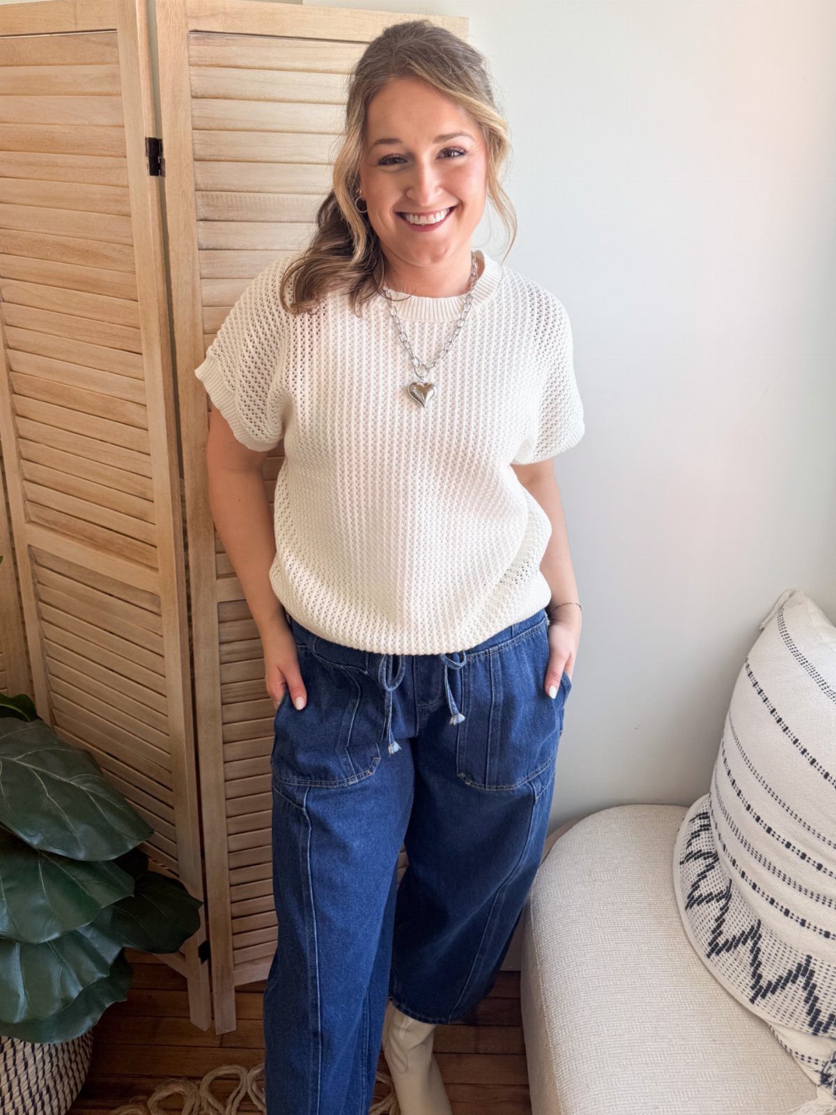 Smiling woman wearing a white short-sleeve knit sweater and dark blue denim trousers.