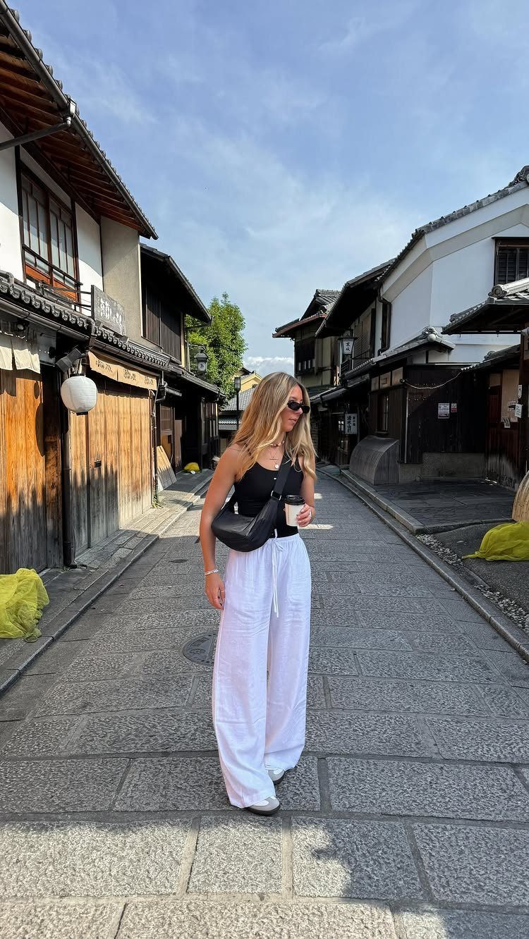 Woman in a black tank top and white wide-leg trousers walking through a traditional street.