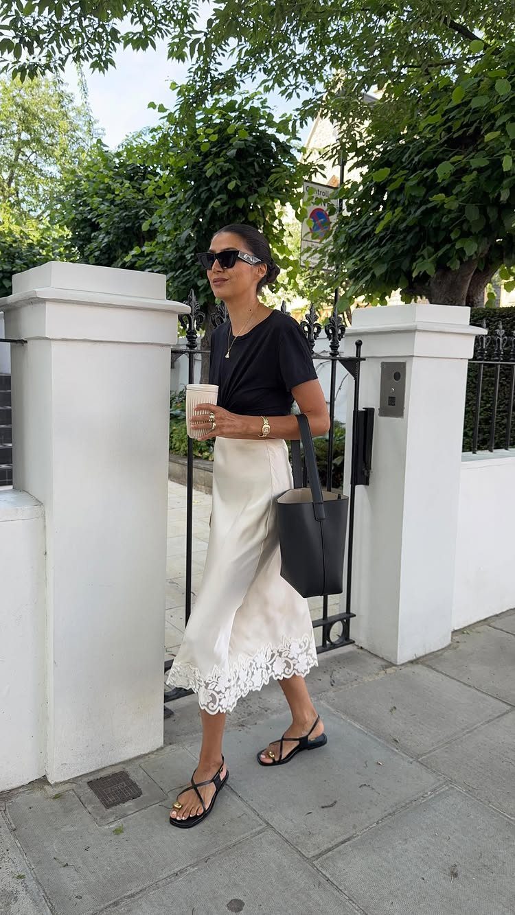 A woman wearing a black crop top and a white lace slip skirt walking outdoors.