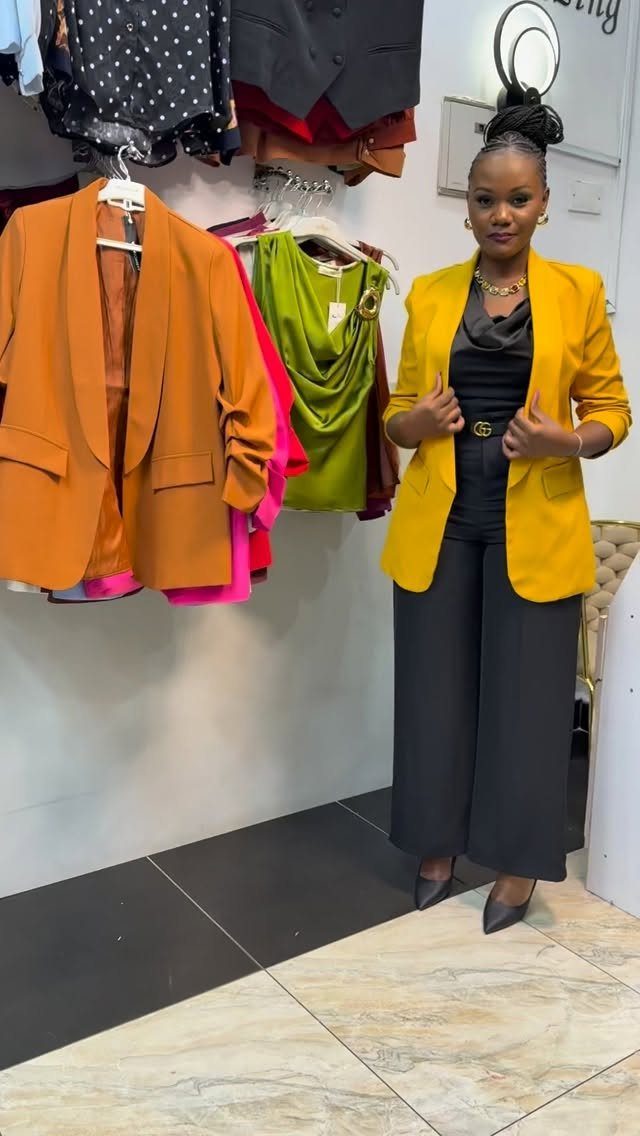 Woman posing in a bright yellow blazer, black top, and wide-leg trousers in a clothing store.