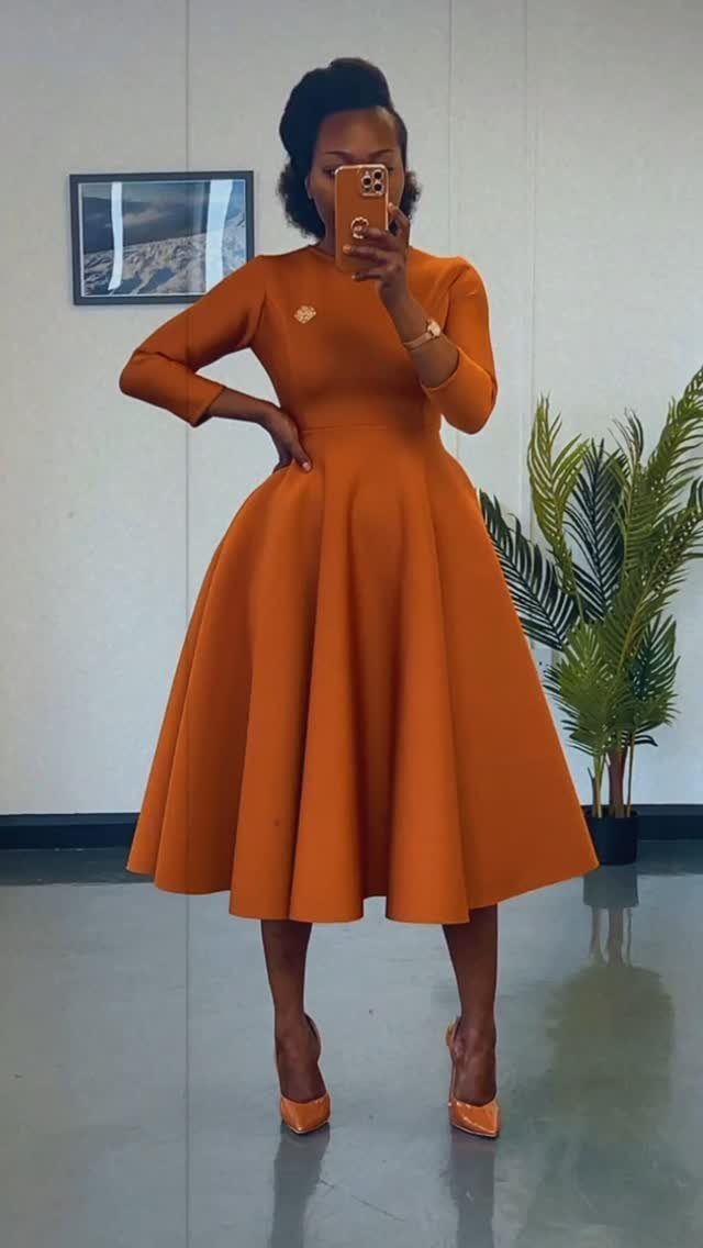 A woman wearing a burnt orange long-sleeved midi dress and matching heels posing for a mirror selfie.