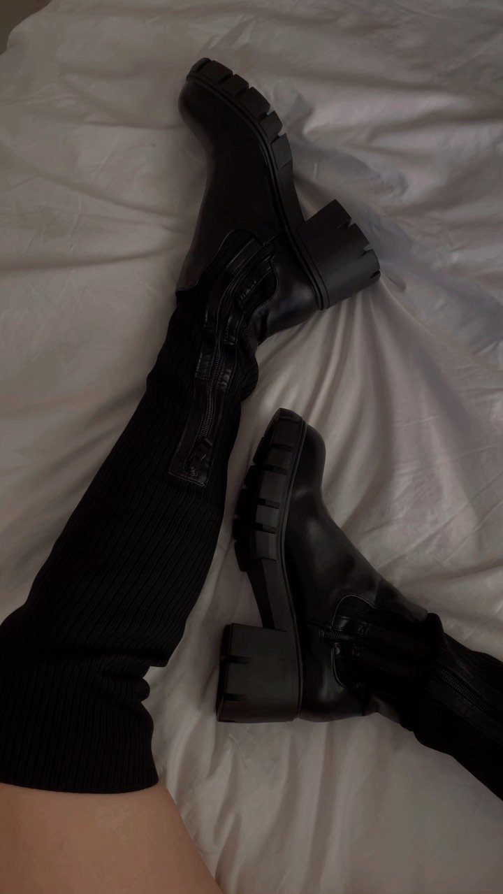 Black chunky-heeled boots with thick lug soles worn with ribbed black socks on white fabric.