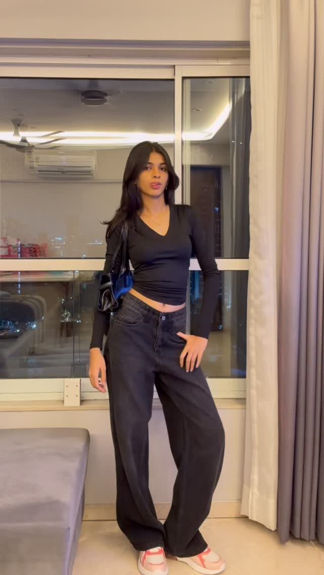 A woman posing in black long-sleeved top and wide-leg black denim jeans.