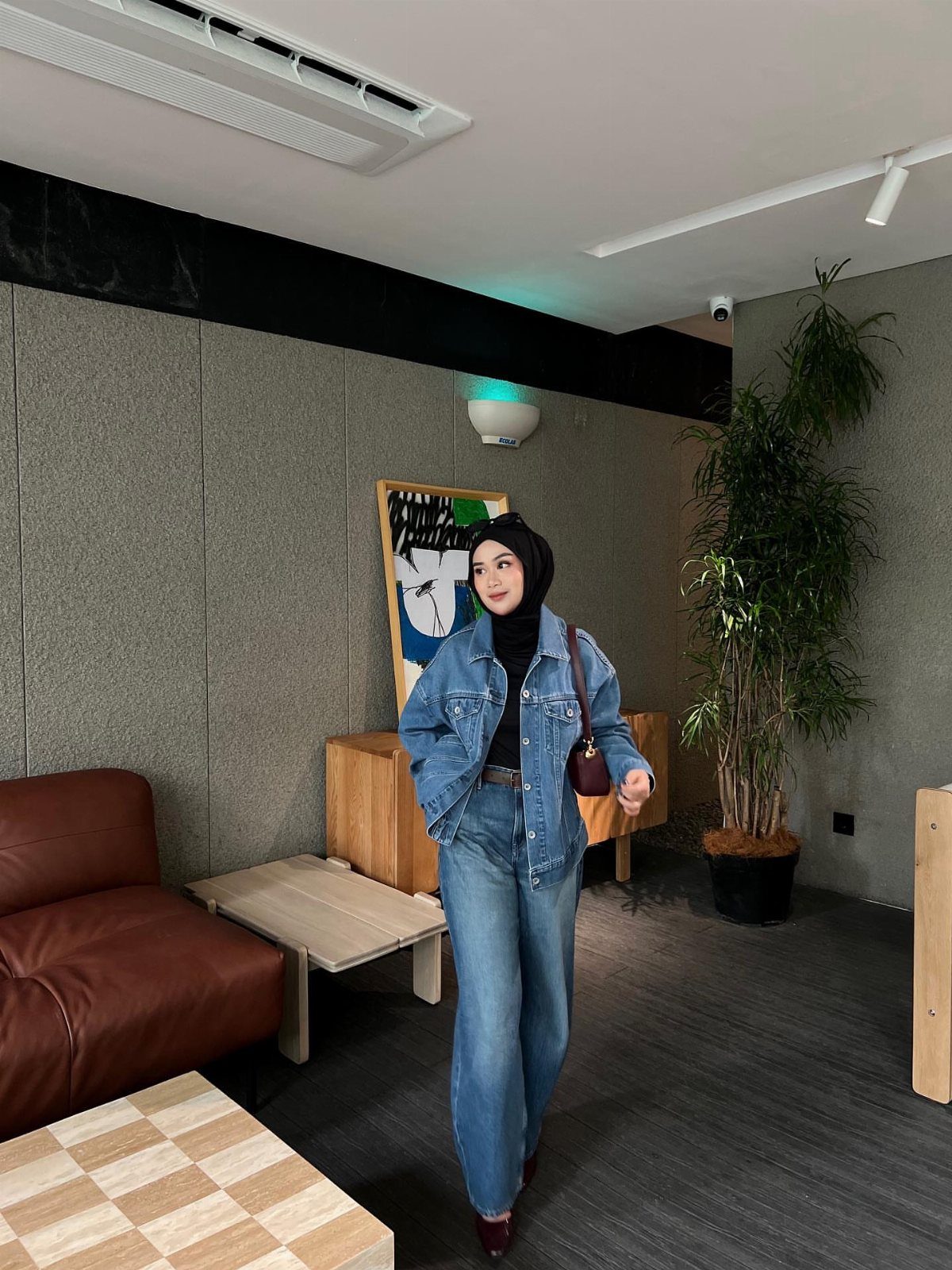A woman posing in a blue denim jacket and matching blue jeans indoors.