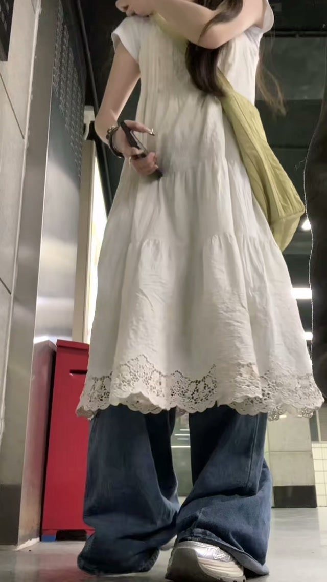 A person wearing a white lace-trimmed boho dress layered over wide-leg mid-wash jeans.